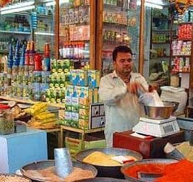 A shop displaying a variety of spices and packaged goods with a man measuring ingredients. - Olive Oil Times