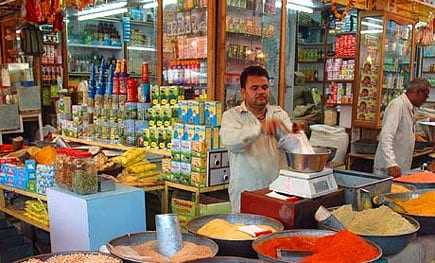 A shop displaying a variety of spices and packaged goods with a man measuring ingredients. - Olive Oil Times