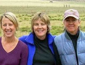 Three women standing together outdoors, smiling at the camera with a grassy background. - Olive Oil Times