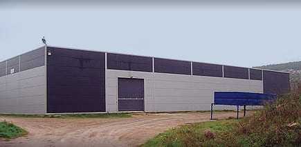 Large industrial warehouse building with a gray and black exterior and a loading dock area. - Olive Oil Times