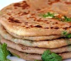 A stack of paratha bread garnished with fresh cilantro leaves on a white plate. - Olive Oil Times