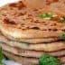 A stack of paratha bread garnished with fresh cilantro leaves on a white plate. - Olive Oil Times