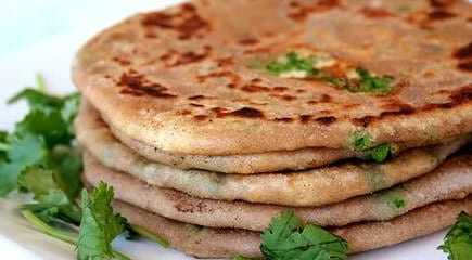 A stack of paratha bread garnished with fresh cilantro leaves on a white plate. - Olive Oil Times