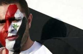 Man with Syrian flag face paint and holding a Syrian flag during a demonstration. - Olive Oil Times