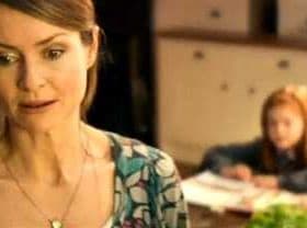 A woman with brown hair wearing a patterned top, looking thoughtfully while a child is seated in the background. - Olive Oil Times