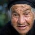 Close-up portrait of an elderly woman wearing a black headscarf and smiling at the camera. - Olive Oil Times