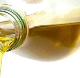 A glass bottle pouring olive oil with a clear stream of liquid flowing from the spout. - Olive Oil Times