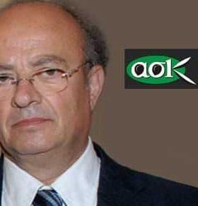 A portrait of a middle-aged man with glasses, wearing a suit and tie, against a neutral background. - Olive Oil Times