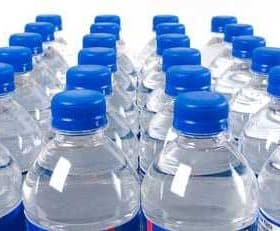 Multiple plastic bottles of water with blue caps arranged in rows. - Olive Oil Times