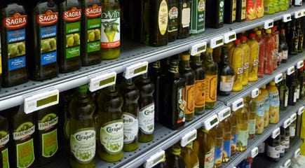 Multiple bottles of olive oil displayed on shelves in a grocery store. - Olive Oil Times