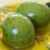 Three green olives resting in a pool of olive oil with leaves nearby. - Olive Oil Times