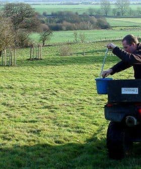 Individual on an ATV pouring material from a bucket while in a grassy field. - Olive Oil Times