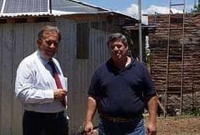 Two men standing outside a building with solar panels on the roof and a wooden structure in the background. - Olive Oil Times