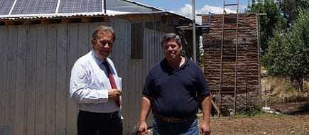 Two men standing outside a building with solar panels on the roof and a wooden structure in the background. - Olive Oil Times