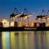 A large container ship named Hapag-Lloyd docked at a port with cranes illuminated at dusk. - Olive Oil Times