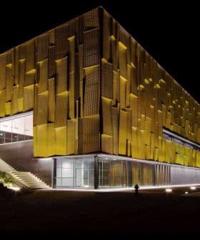 Contemporary building featuring a yellow facade with a textured surface, illuminated at night. - Olive Oil Times