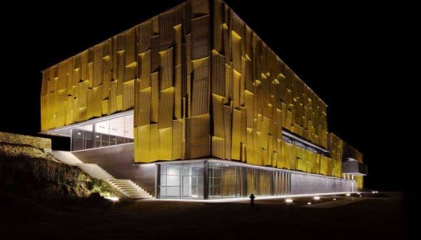 Contemporary building featuring a yellow facade with a textured surface, illuminated at night. - Olive Oil Times