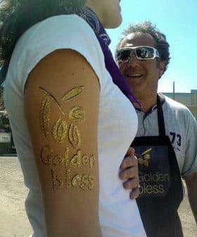 A person's arm with golden body art displaying the text 'Golden Bless'. - Olive Oil Times