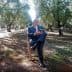 A man in a suit sitting on a wooden chair in an olive grove surrounded by trees. - Olive Oil Times
