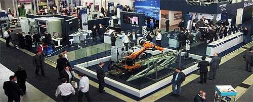 An exhibition booth featuring a robotic arm and various displays with attendees interacting. - Olive Oil Times