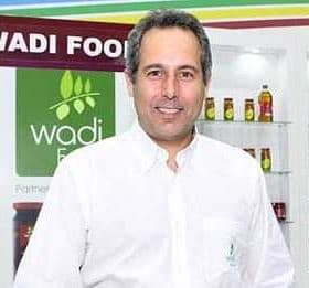 Man in a white shirt standing in front of Wadi Food branding and product display. - Olive Oil Times