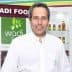 Man in a white shirt standing in front of Wadi Food branding and product display. - Olive Oil Times