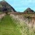 A grassy pathway bordered by fences leading towards two hills in Otago, New Zealand. - Olive Oil Times
