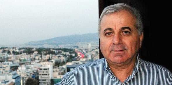 A man with gray hair wearing a striped shirt, posing for a portrait with a cityscape in the background. - Olive Oil Times