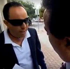 Two men talking outside, one wearing sunglasses and a dark suit, the other in a suit and tie. - Olive Oil Times