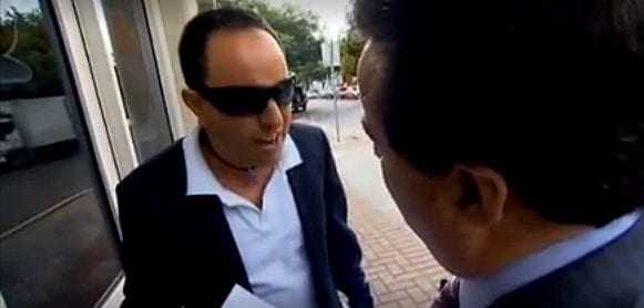 Two men talking outside, one wearing sunglasses and a dark suit, the other in a suit and tie. - Olive Oil Times