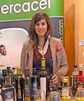 Woman standing behind a table with various bottles of olive oil at an exhibition booth. - Olive Oil Times