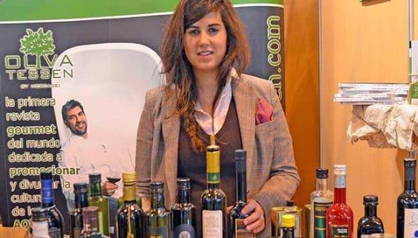 Woman standing behind a table with various bottles of olive oil at an exhibition booth. - Olive Oil Times