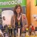 Woman standing behind a table with various bottles of olive oil at an exhibition booth. - Olive Oil Times