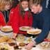 Three individuals selecting food from a buffet table with various dishes and plates. - Olive Oil Times