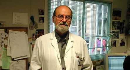 A man wearing a white lab coat stands in an office with a computer and various papers around. - Olive Oil Times