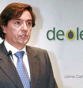 Man in a suit speaking at a presentation with Deoleo logo in the background. - Olive Oil Times
