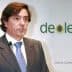 Man in a suit speaking at a presentation with Deoleo logo in the background. - Olive Oil Times