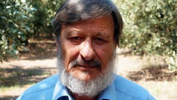 A man with a beard wearing a blue shirt, standing in an olive grove. - Olive Oil Times