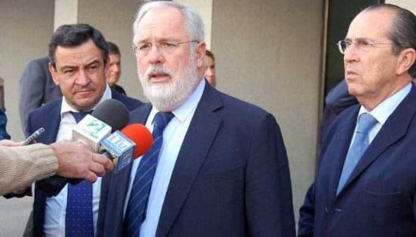 Three men at a press conference, one speaking into microphones while the others listen attentively. - Olive Oil Times