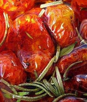 Close-up of oven dried tomatoes submerged in olive oil with rosemary sprigs. - Olive Oil Times