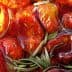 Close-up of oven dried tomatoes submerged in olive oil with rosemary sprigs. - Olive Oil Times