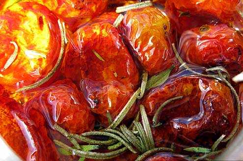 Close-up of oven dried tomatoes submerged in olive oil with rosemary sprigs. - Olive Oil Times
