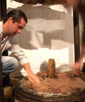 Man using a traditional olive oil press, working with the grinding mechanism and olives. - Olive Oil Times
