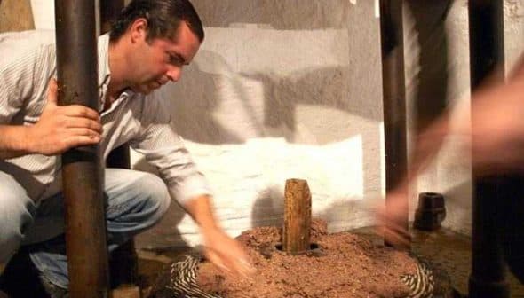 Man using a traditional olive oil press, working with the grinding mechanism and olives. - Olive Oil Times