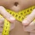 Person holding a yellow tape measure around their waist, showing measurement of body size. - Olive Oil Times
