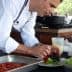 Chef in a white coat arranging salad ingredients on a plate during a cooking demonstration. - Olive Oil Times