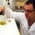 Scientist in a lab coat pouring olive oil from a bottle into a beaker in a laboratory setting. - Olive Oil Times