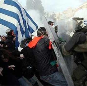 A protest scene in Greece featuring a person holding a Greek flag and police in riot gear. - Olive Oil Times