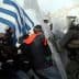A protest scene in Greece featuring a person holding a Greek flag and police in riot gear. - Olive Oil Times