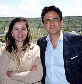 Two individuals standing together outdoors, smiling at the camera with a landscape in the background. - Olive Oil Times